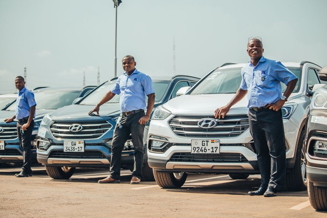 Three PTL drivers in uniform standing beside a line of company SUVs